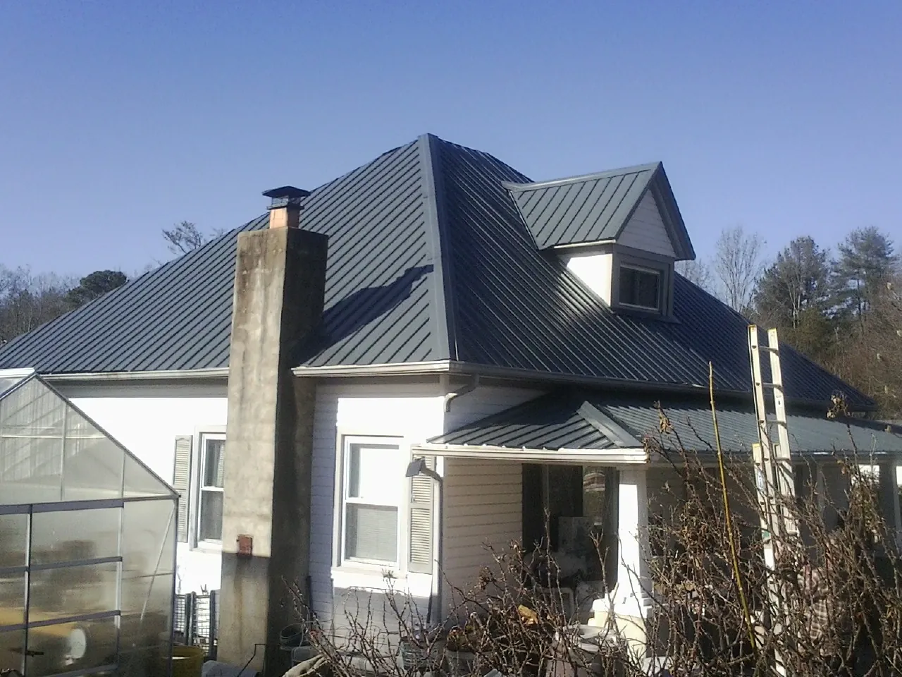 Dark blue standing seam metal roof on a white farmhouse with dormer — Slate & Tile Roof Repair by Roofing Brothers in Prichard