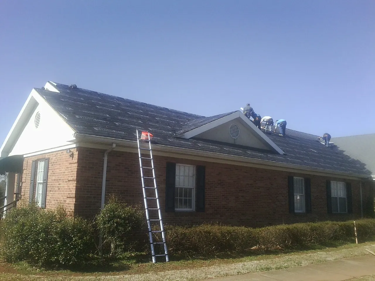 Crew tearing shingles off a brick ranch roof with a ladder set — Emergency Roof Repair work by our crew in Prichard