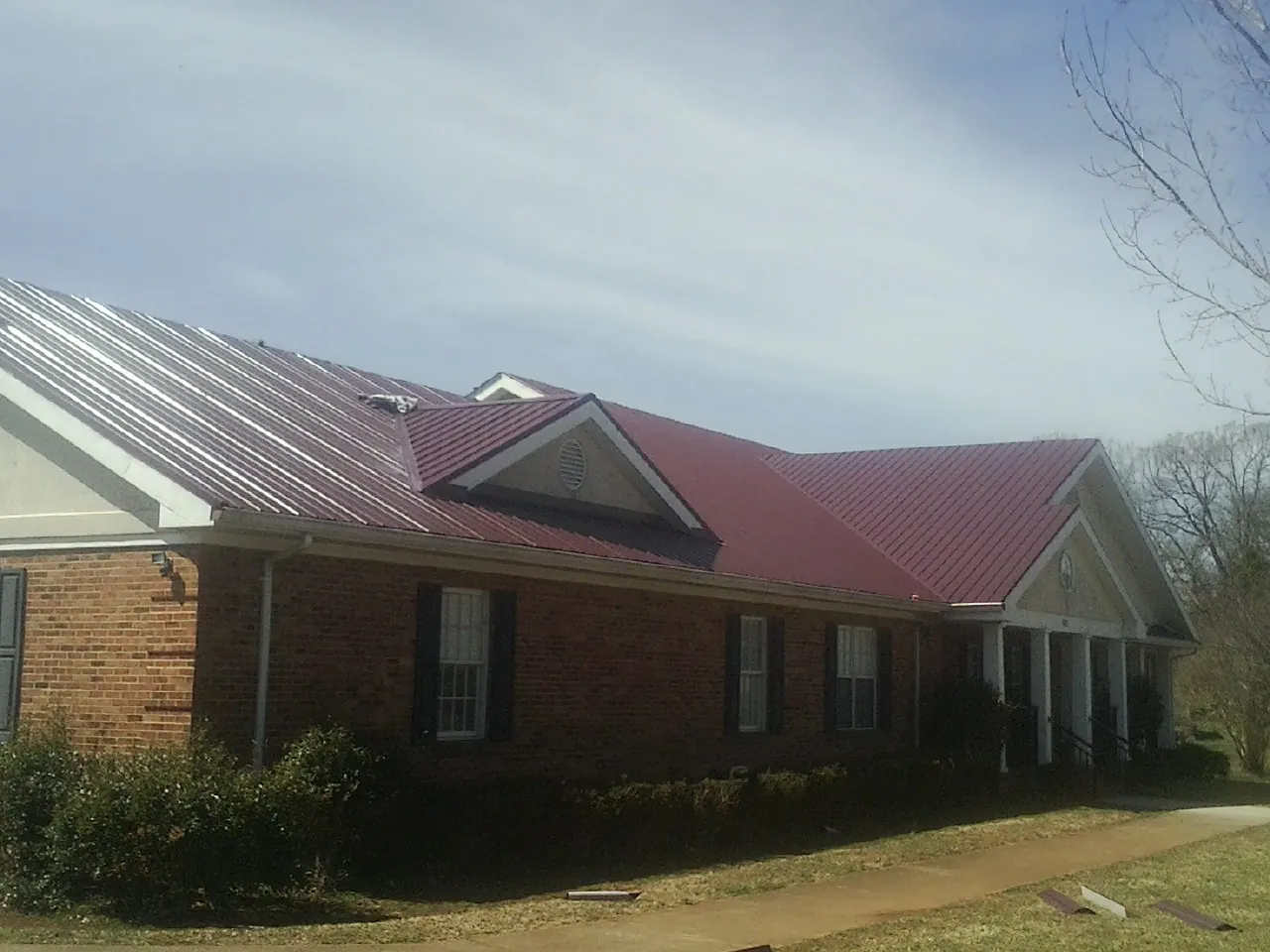 Red metal roof with gabled entries on a long brick building, from a Hail Damage Roof Repair job in Prichard