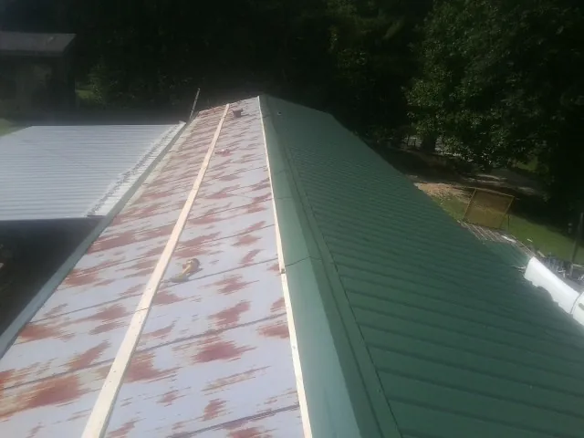 Old rusted panels beside newly installed green metal roofing — Wind Damage Roof Repair by Roofing Brothers in Prichard