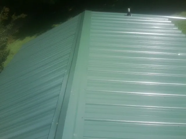 New green metal panels meeting at the ridge of a roof — Flat Roof Repair work by our crew in Prichard