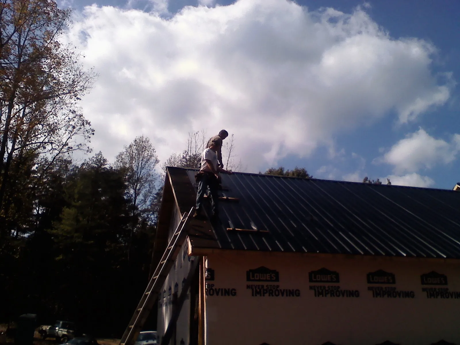 Roofer fastening dark metal panels high against a cloudy sky, from a Roof Inspection job in Prichard