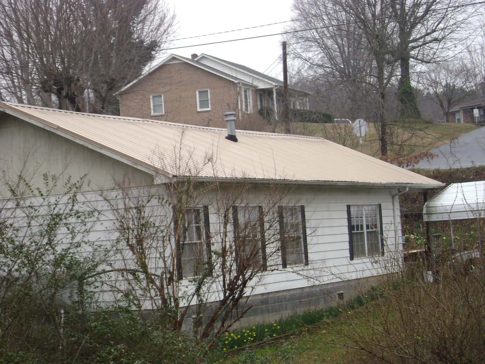 Tan metal roof on a white sided house set into a hillside — Commercial Roofing by Roofing Brothers in Prichard